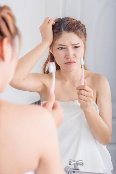 unhappy woman in bath towel brushing teeth with mirror in bathro