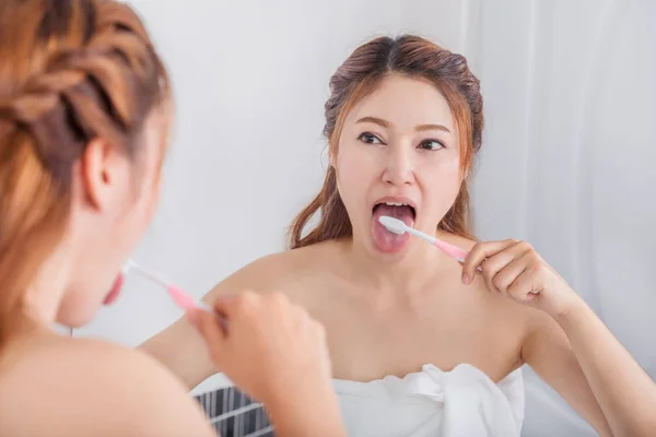 Woman cleaning tongue using toothbrush with mirror in bathroom — Stock Photo, Image