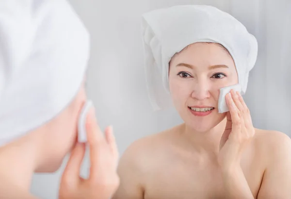 Vrouw op zoek spiegel en reinigen van haar gezicht met katoen — Stockfoto