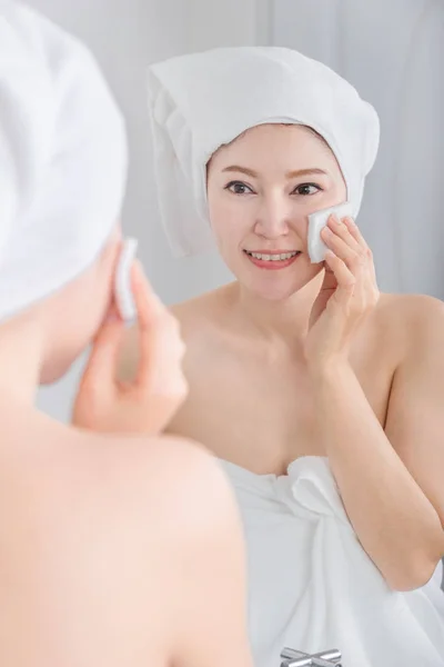 Femme regarder miroir et nettoyer son visage avec du coton — Photo