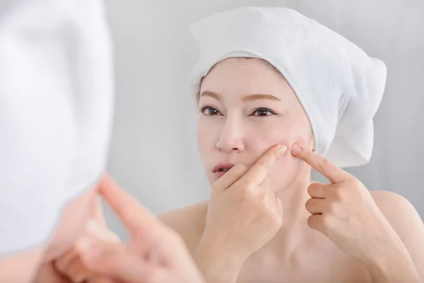 Woman squeezing pimple in front of mirror — Stock Photo, Image