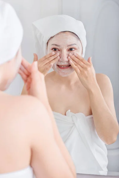 Femme appliquant un masque sur son visage et regardant dans le miroir — Photo