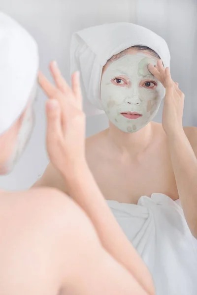 Femme appliquant un masque sur son visage et regardant dans le miroir — Photo