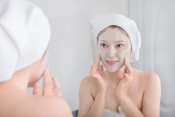Femme appliquant un masque sur son visage et regardant dans le miroir — Photo