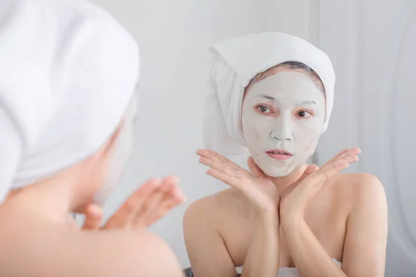 Woman applying mask on her face and looking in the mirror — Stock Photo, Image