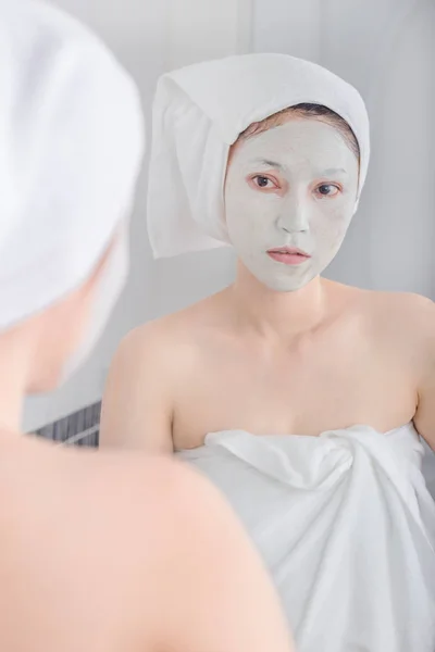 Mulher aplicando máscara em seu rosto e olhando no espelho — Fotografia de Stock