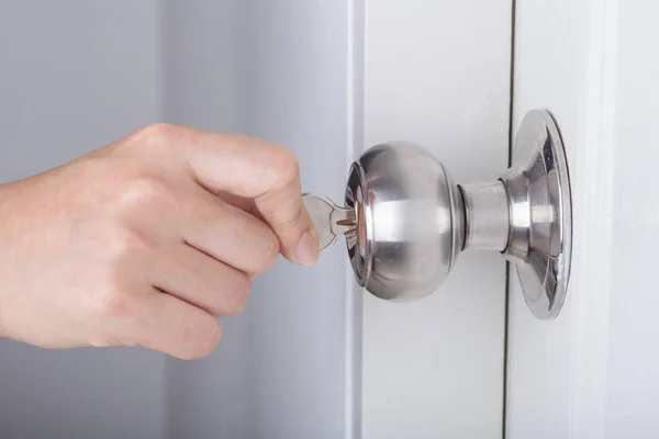 Mâna folosește cheia pentru deblocarea butonului ușii pe ușa albă — Fotografie, imagine de stoc