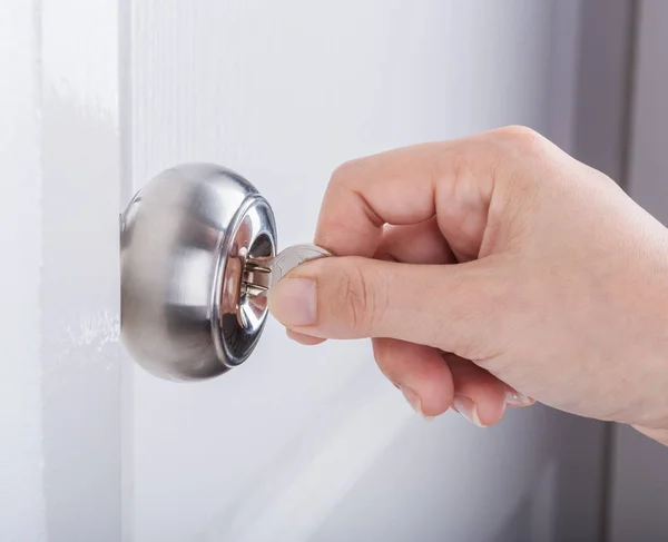 Mano utilizar la llave para desbloquear la perilla de la puerta en la puerta blanca — Foto de Stock