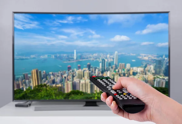 Mano que sostiene el control remoto del televisor con una pantalla de televisión y ciudad — Foto de Stock