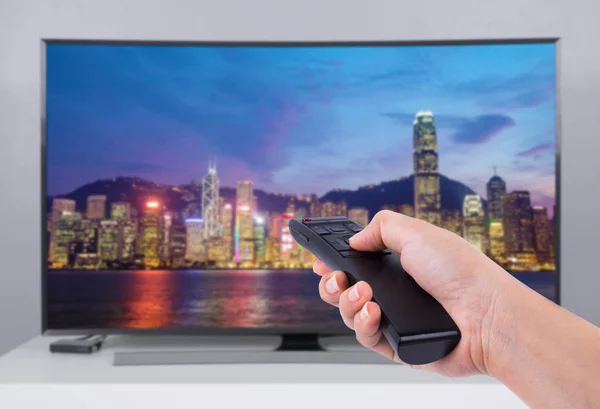 Mão segurando o controle remoto de Tv com uma tela de televisão e cidade — Fotografia de Stock