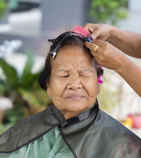 Hand of a hairstylist doing a perm rolling hair of senior woman — Stock Photo, Image