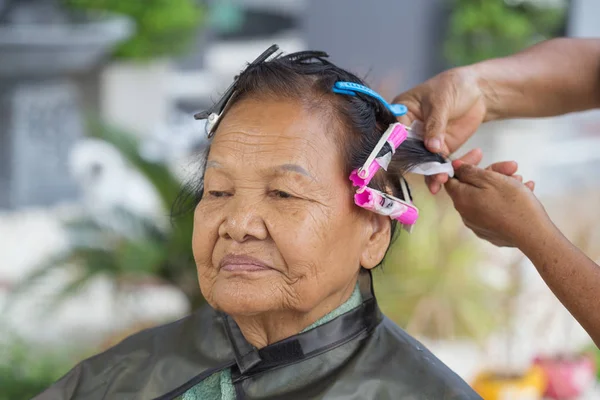 Hand of a hairstylist doing a perm rolling hair of senior woman — Stock Photo, Image