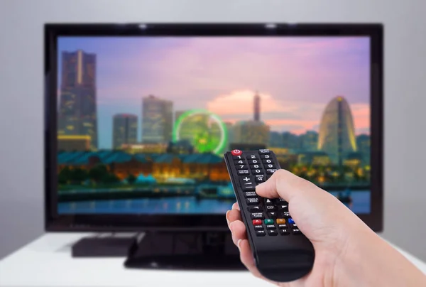 Hand met de afstandsbediening van de Tv met een scherm televisie en stad — Stockfoto