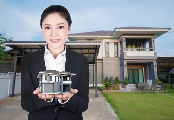 Model huis in zakelijke vrouw hand met de werkelijke huis en tuin — Stockfoto