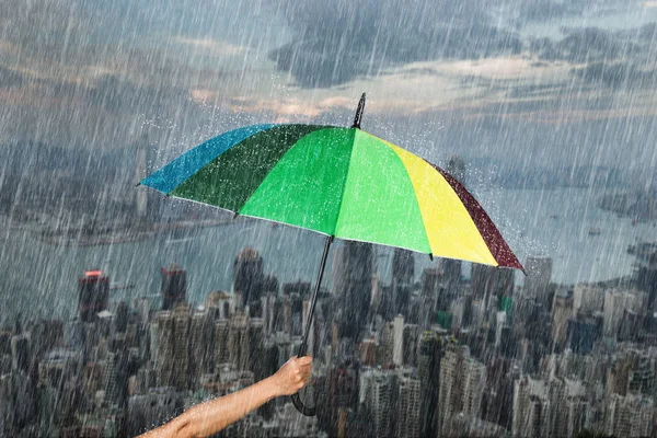 Mano sosteniendo paraguas multicolor con lluvia en la ciudad — Foto de Stock