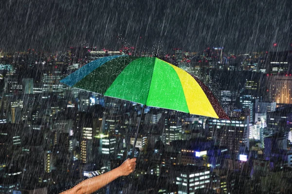 Main tenant parapluie multicolore avec chute de pluie en ville — Photo