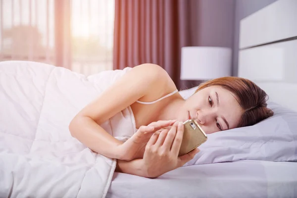 Femme utilisant son smartphone sur le lit dans la chambre à coucher avec une lumière douce — Photo
