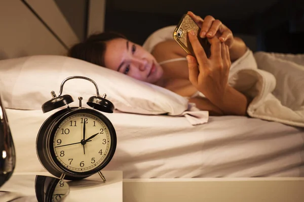 Horloge montrent 2 heures et femme en utilisant son smartphone sur le lit en th — Photo