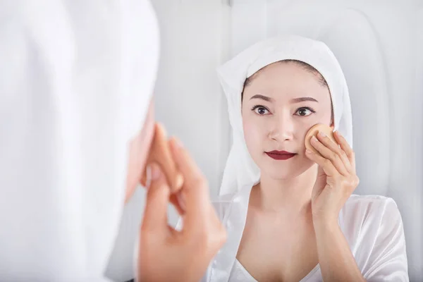 女人看镜子和应用在脸上的粉底 — 图库照片