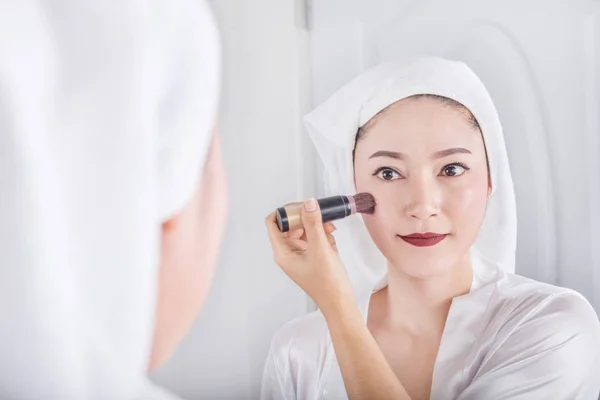 Donna che si guarda allo specchio e applica cosmetici con la spazzola — Foto Stock