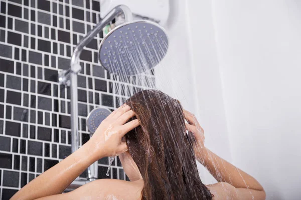 Femme se lave les cheveux et le visage sous la douche à effet pluie, vue arrière — Photo