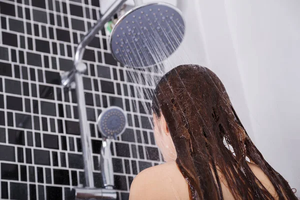 Mulher está lavando seu cabelo e rosto pelo chuveiro de chuva, visão traseira — Fotografia de Stock