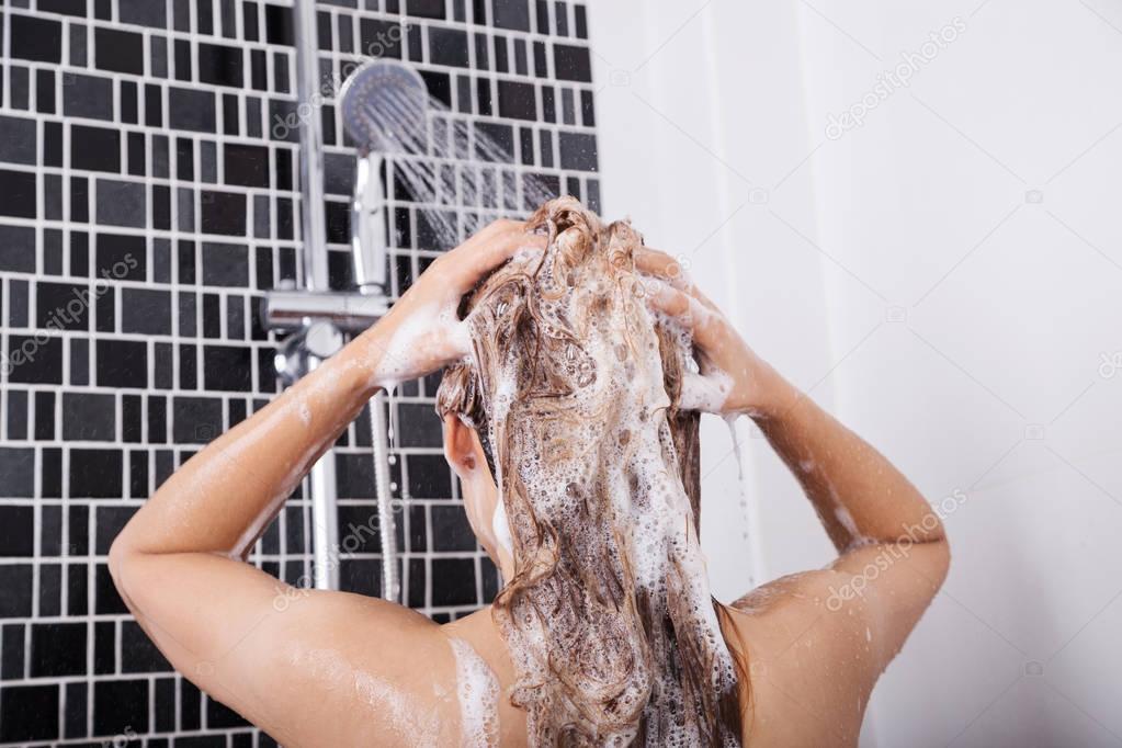 woman washing head and hair in the shower by shampoo, rear view