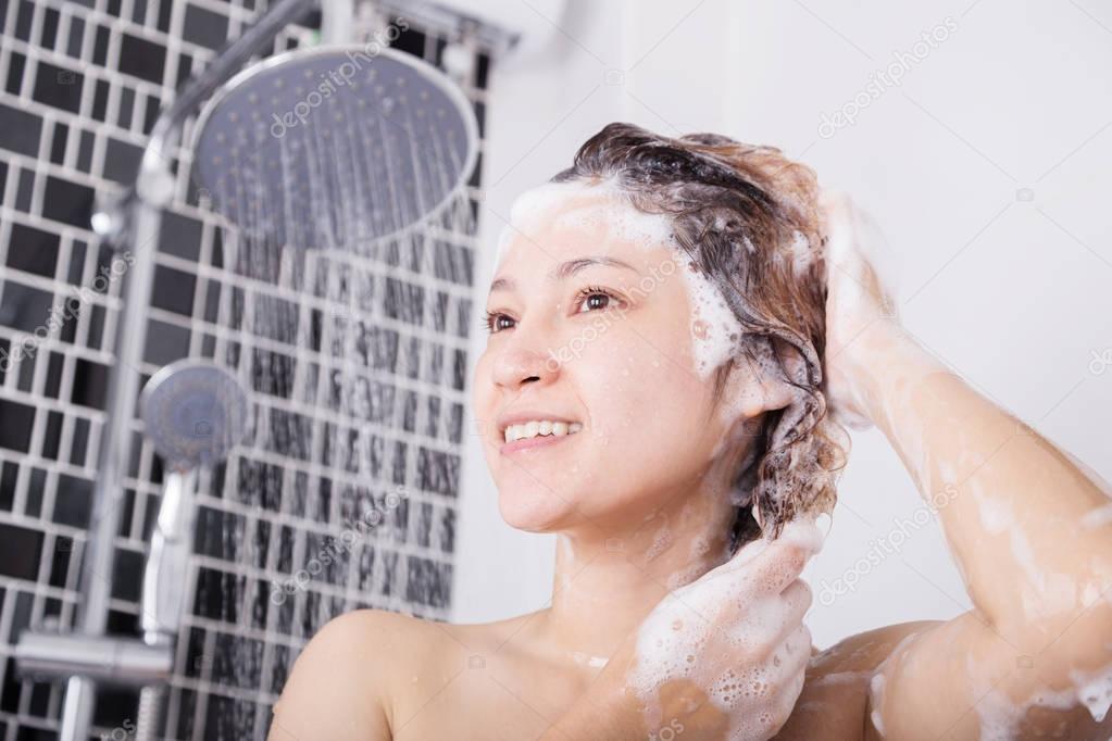 happy woman washing head with shampoo and shower