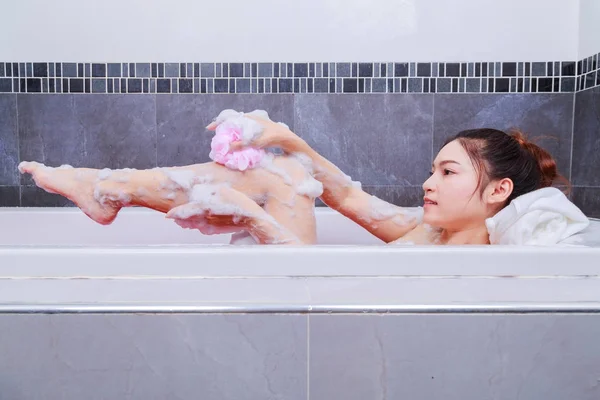 Mujer lavando pierna con esponja en bañera en el baño —  Fotos de Stock
