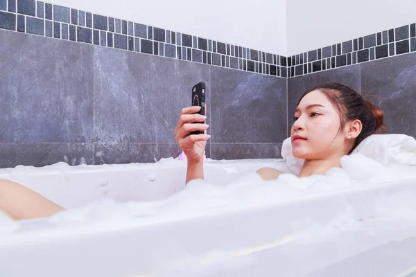 Kobieta przy użyciu telefonu komórkowego w wanna w łazience — Zdjęcie stockowe