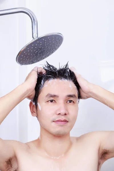 Mies on sateessa suihku ja pesu hiukset kylpyhuoneessa — kuvapankkivalokuva