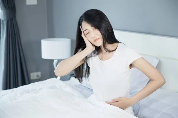 Woman stomach pain and headache on her bed in bedroom