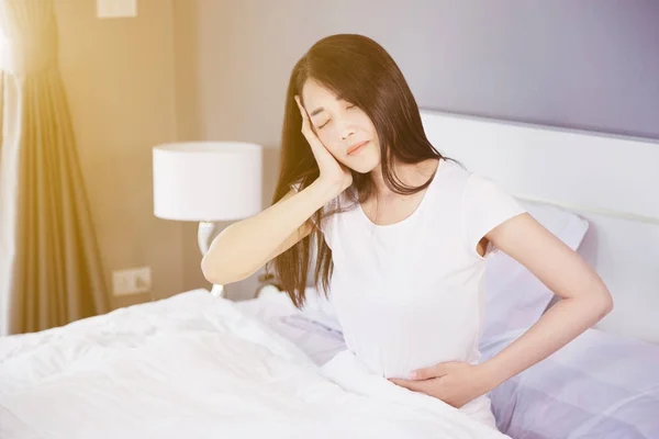 Woman stomach pain and headache on her bed in bedroom — Stock Photo, Image