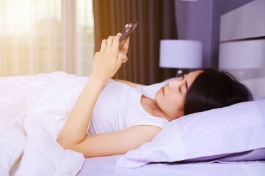 yatak yatak odasında elinde bir telefon kullanan kadın