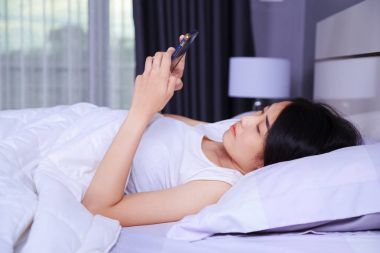yatak yatak odasında elinde bir telefon kullanan kadın