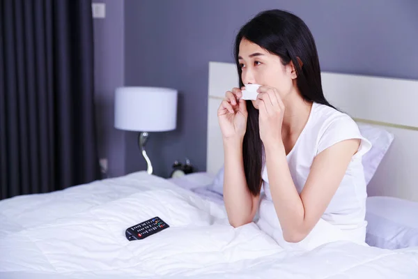 Wanita menangis sambil menonton TV dengan remote di tempat tidur di kamar tidur — Stok Foto