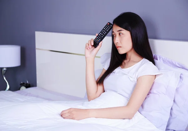 Wanita dengan remote control di tempat tidur di kamar tidur — Stok Foto