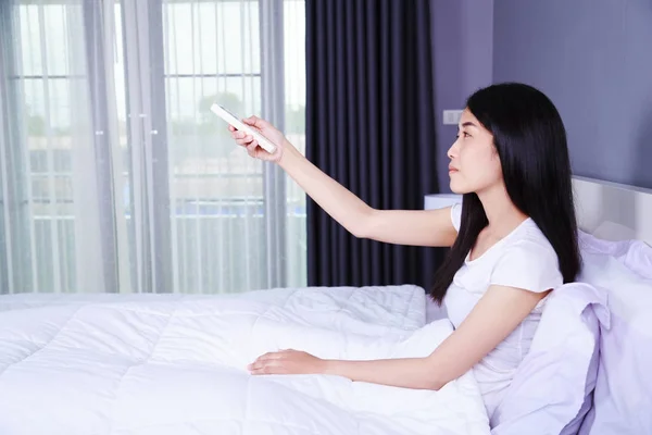 Femme main tenir climatiseur à distance sur le lit dans la chambre — Photo