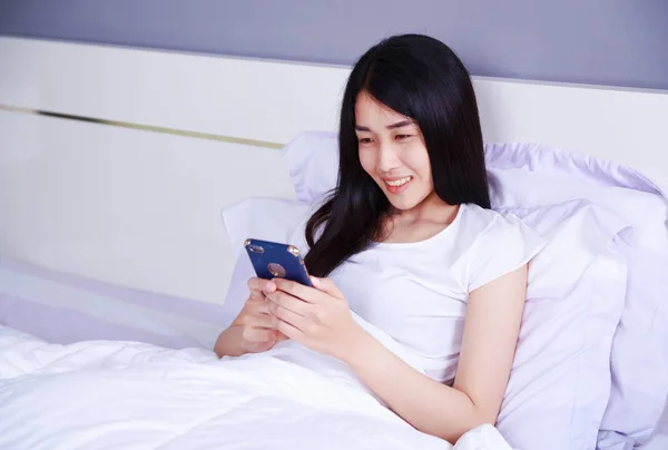 Femme heureuse en utilisant un téléphone dans sa main sur le lit dans la chambre — Photo