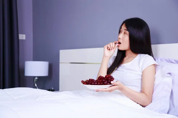 Женщина с красным виноградом на кровати в спальне — стоковое фото