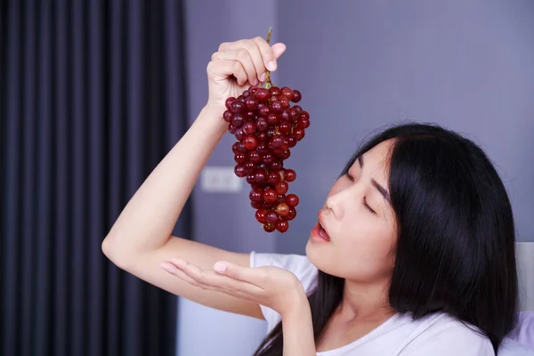 Woman with red grape on bed in bedroom — Stock Photo, Image