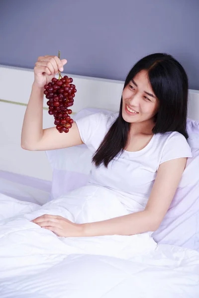 Woman with red grape on bed in bedroom — Stock Photo, Image