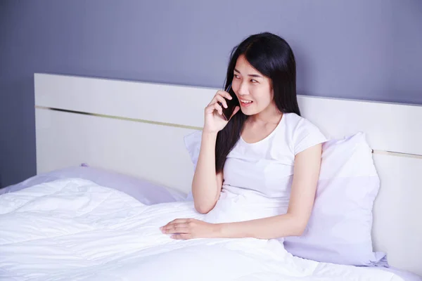Wanita berbicara di ponsel di tempat tidur di kamar tidur — Stok Foto