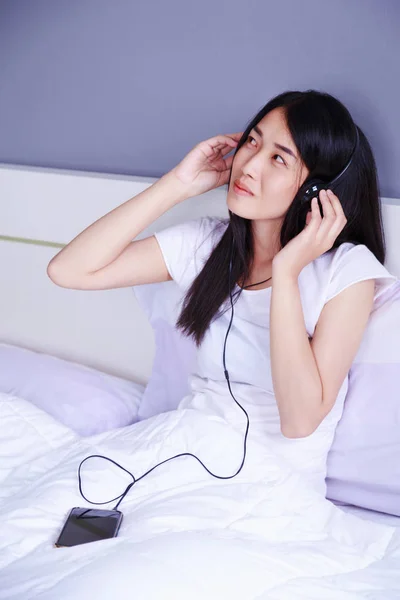 Femme dans les écouteurs écouter de la musique de smartphone sur le lit dans — Photo