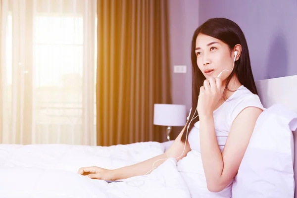 Mujer usando auriculares en el teléfono móvil en la cama en el dormitorio — Foto de Stock