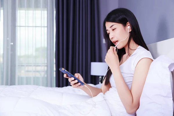 Femme utilisant un écouteur sur téléphone portable au lit dans la chambre — Photo