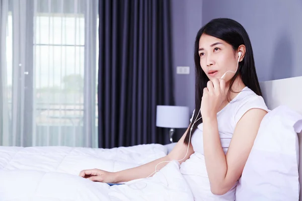 Mujer usando auriculares en el teléfono móvil en la cama en el dormitorio — Foto de Stock