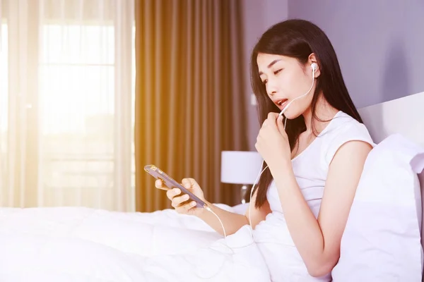 Femme utilisant un écouteur sur téléphone portable au lit dans la chambre — Photo