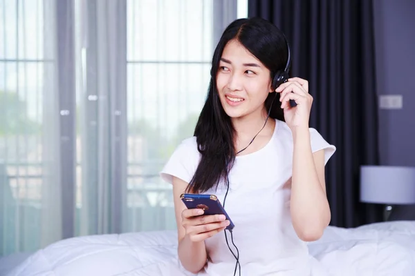 Frau mit Kopfhörer hört Musik vom Smartphone im Bett — Stockfoto