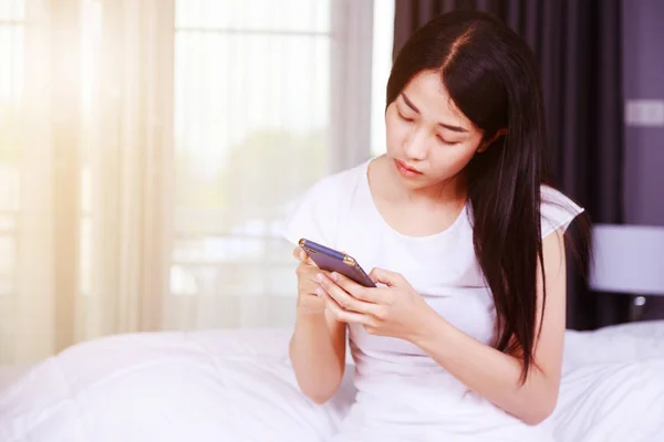 Femme heureuse en utilisant un téléphone dans sa main sur le lit dans la chambre — Photo